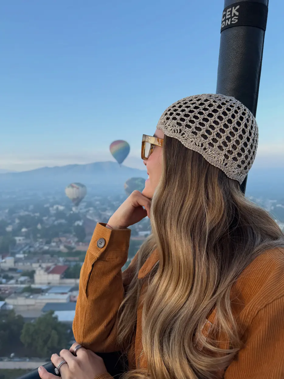 Mujer de perfil en la canasta junto a la vela de colores de un globo aerostático en Teotihuacán